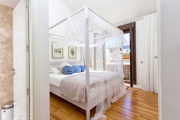 A bedroom with a canopy bed, a wooden floor, and a view of the outside. - Kim - Holiday Penthouse Malaga City (Málaga)