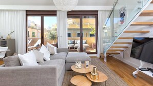A modern living room with a grey sectional sofa, a glass staircase, and a large chandelier. - Kim - Holiday Penthouse Malaga City (Málaga)