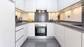 A modern kitchen with white cabinetry, stainless steel appliances, and a central island with fruit.
