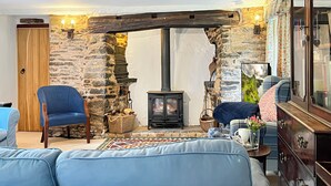 A cozy room with a stone wall, a wooden door, a blue armchair, a sofa, a fireplace, and a large mirror. - Bratton Mill Farmhouse, Bratton Fleming (Bratton Fleming)