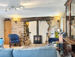 A cozy room with a stone wall, a wooden door, a blue armchair, a sofa, a fireplace, and a large mirror.