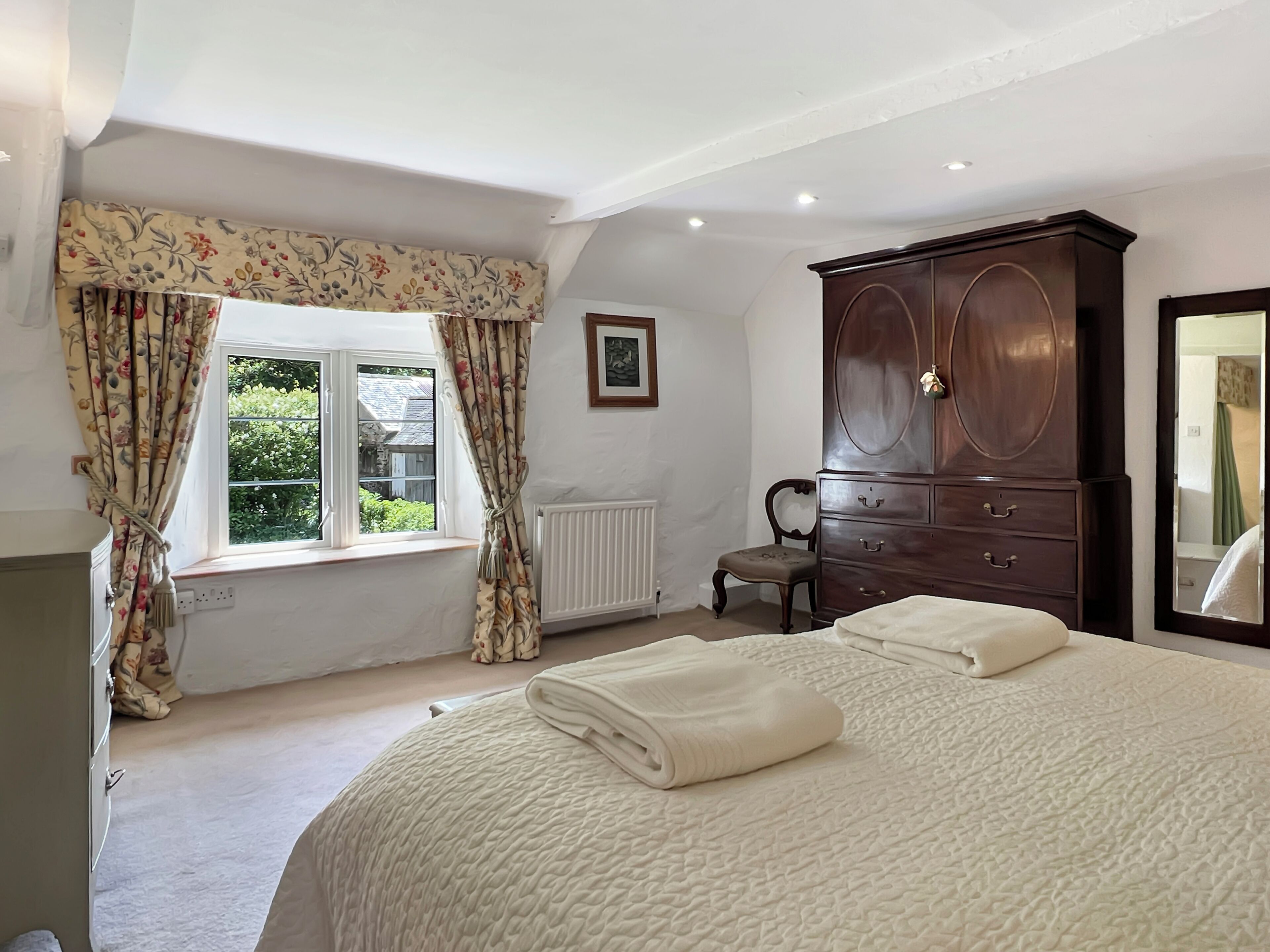 A bedroom with a bed, a dresser, a chair, a window with curtains, and a radiator.