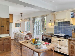A kitchen with wooden cabinets, a dining table with chairs, a stove, and a window with curtains.