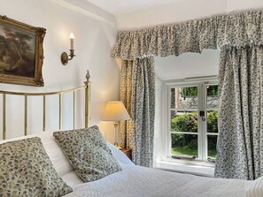 A bedroom with a bed, a nightstand, a lamp, a window with curtains, and a painting on the wall.