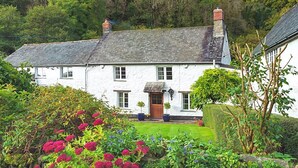 A white house with a sloped roof, a front door, and a small porch with potted plants. - Bratton Mill Farmhouse, Bratton Fleming (Bratton Fleming)