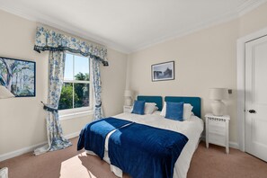 A bedroom with a bed, two bedside tables, a window with curtains, a door, and a wall-mounted picture.