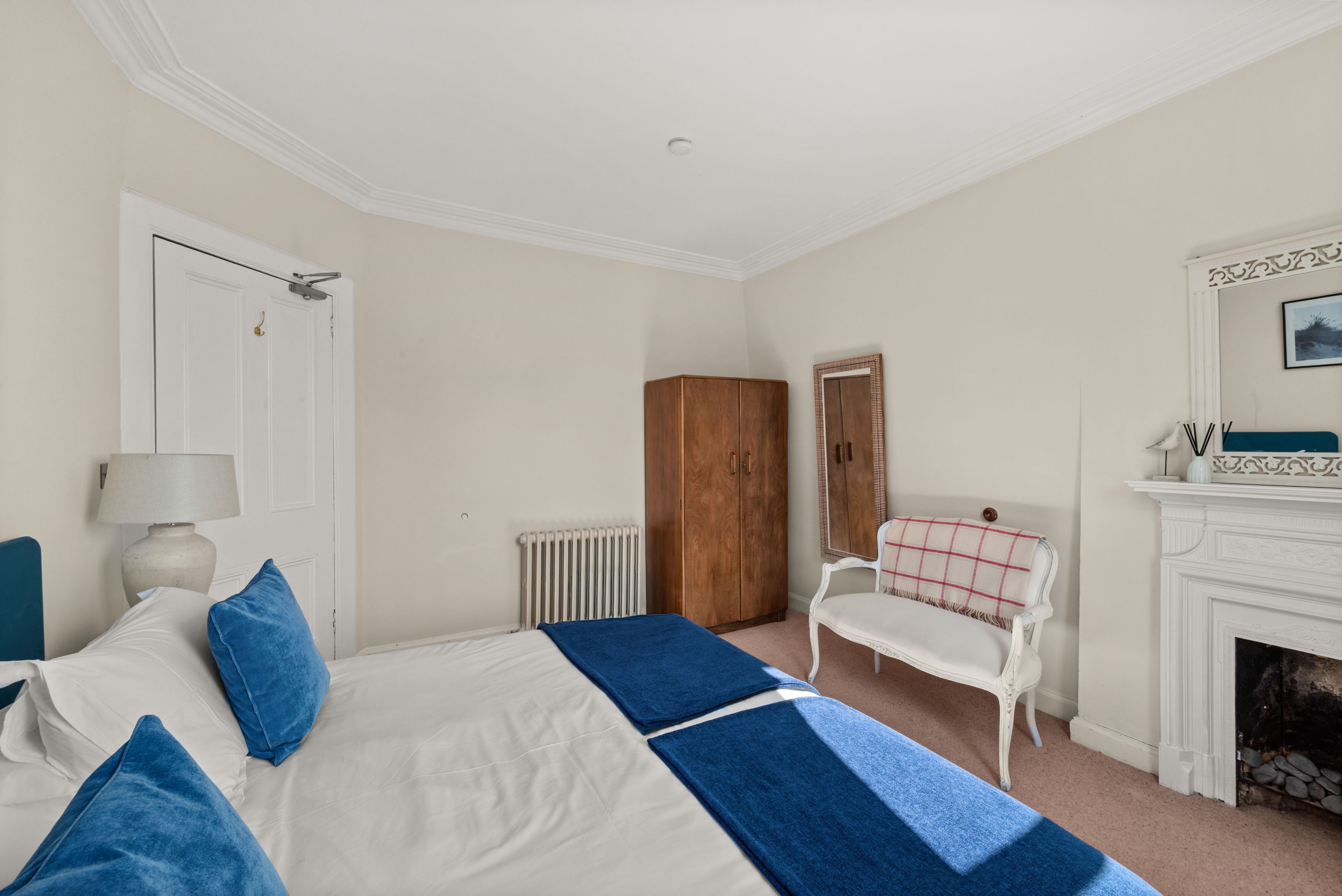 A bedroom with a bed, a chair, a radiator, a wardrobe, and a fireplace.