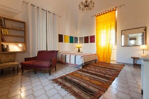 Una habitación con una cama, una silla, una estantería, una alfombra y un espejo.