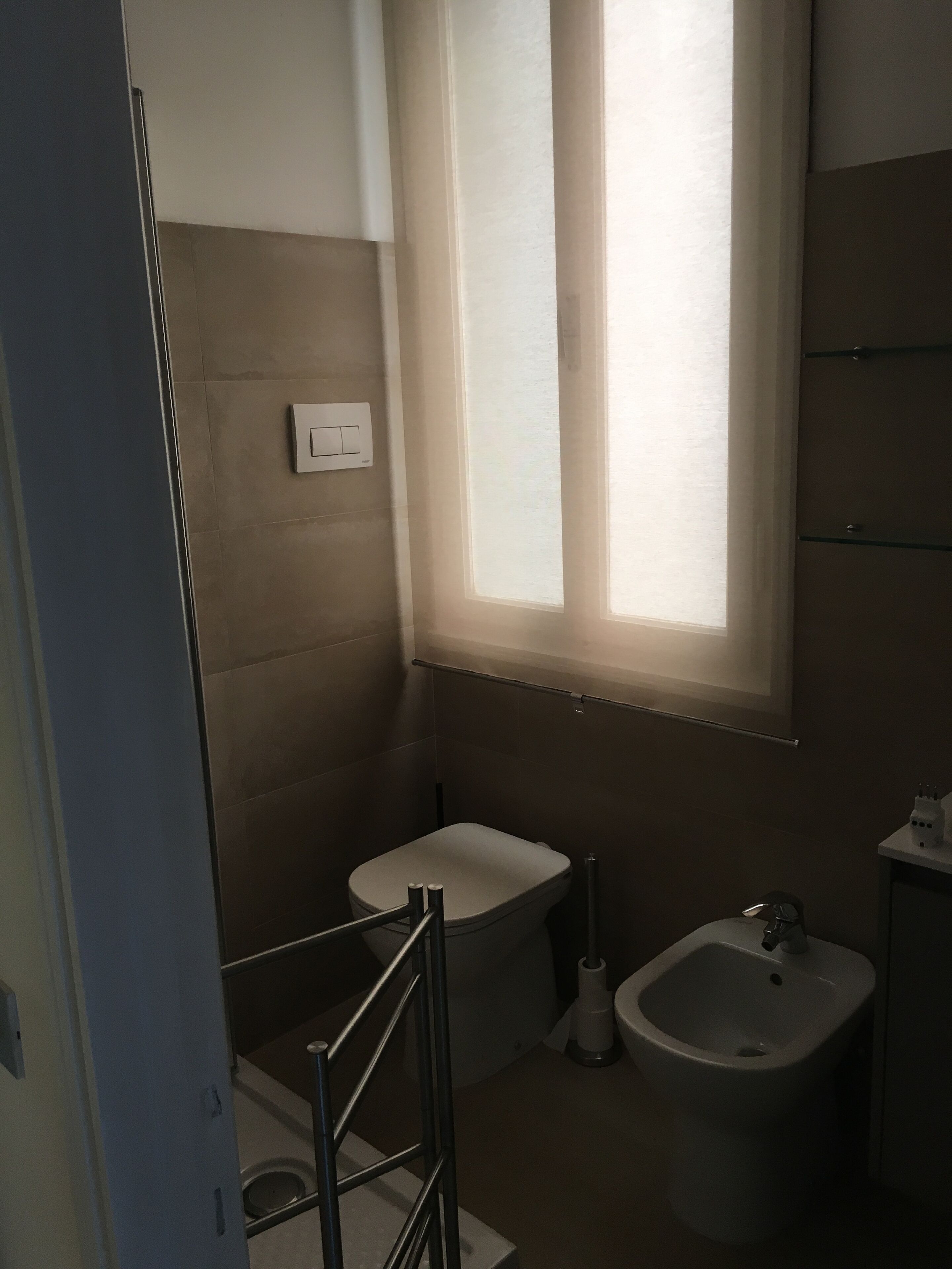 A bathroom with a toilet, bidet, and a window.