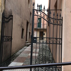 Une ruelle étroite, avec un portail en fer forgé, un chemin pavé et des bâtiments dotés de balcons.