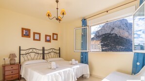 A bedroom with a bed, bedside tables, a lamp, framed pictures on the wall, and a window with a mountain view. - Apolo XVIII 57 - Grupo Turis - Calpe, Costa Blanca (Calpe)