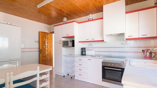 Une cuisine compacte avec des meubles blancs, un four à micro-ondes, une machine à café et une cuisinière.