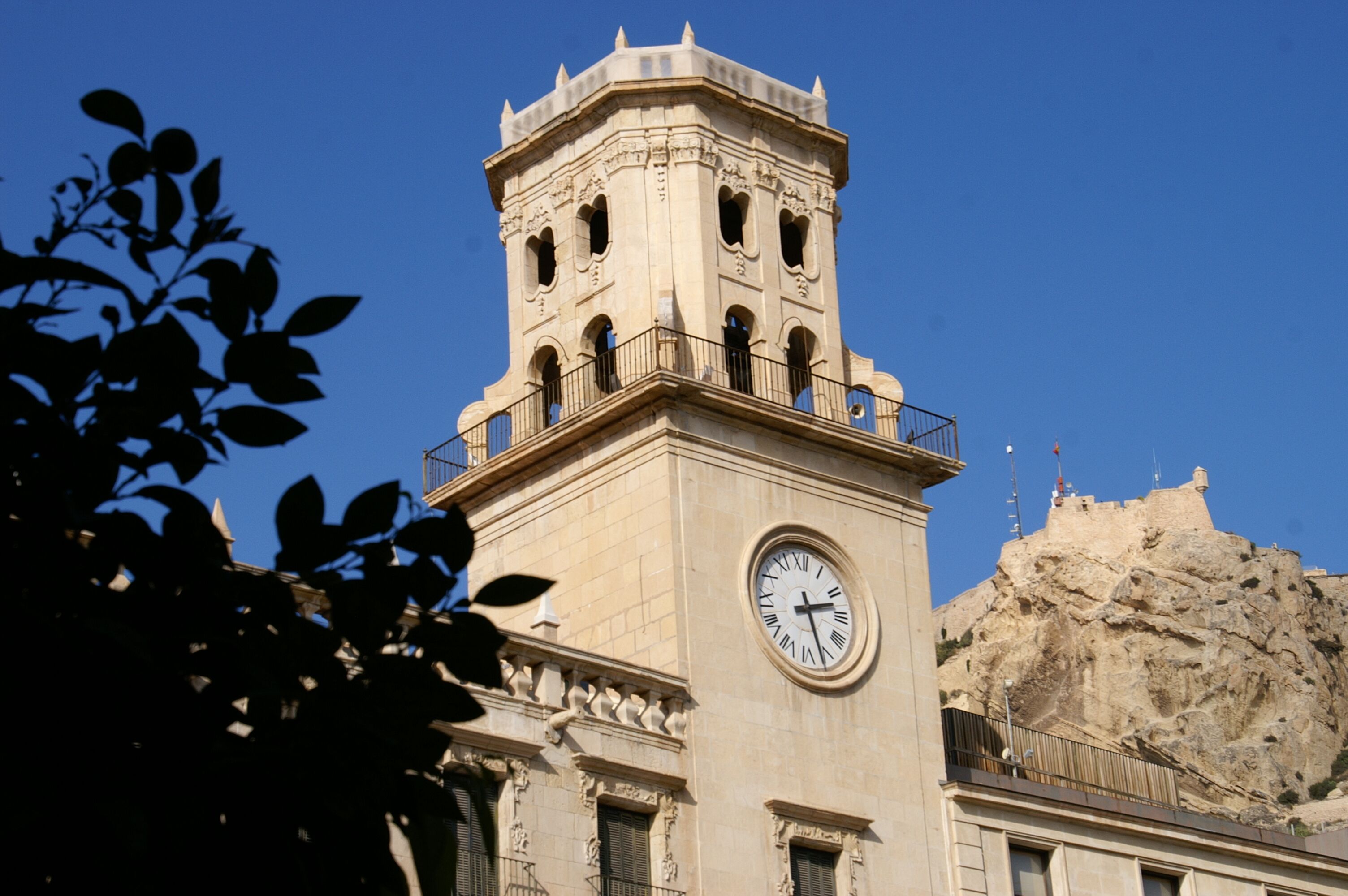 A clock tower with a balcony, set against a clear blue sky.