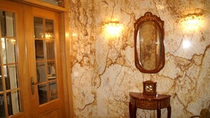 Una stanza con una porta in legno, un muro di marmo, uno specchio e un tavolino con un orologio.