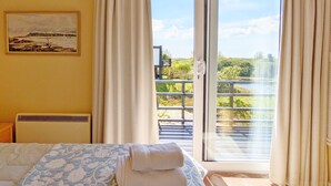 Un dormitorio con cama, un cuadro en la pared y vistas a un balcón con barandilla y vegetación.