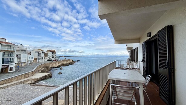 Un balcón con vista al mar, un muro de piedra y edificios al fondo.