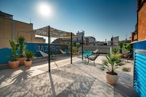 A rooftop terrace with potted plants, outdoor seating, and a clear blue sky.