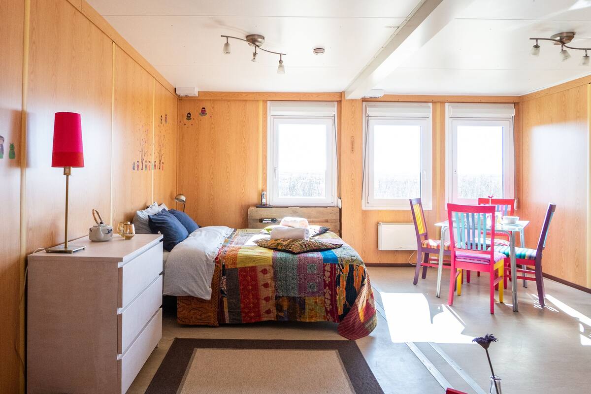 A bedroom with a bed, dresser, lamp, and a small table with chairs.