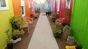Um deck de madeira estreito com cadeiras de vime e plantas em vasos, que conduz a uma porta central.