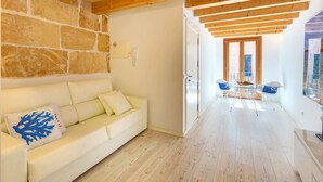 A modern interior with a stone wall, a white sofa with blue cushions, and a wooden floor. - URBAN SUITES 2 PALMA STANDARD by PriorityVillas (Palma de Mallorca)