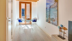 A modern interior with a wooden ceiling, a glass table with chairs, and a large painting of a coastal scene. - URBAN SUITES 2 PALMA STANDARD by PriorityVillas (Palma de Mallorca)