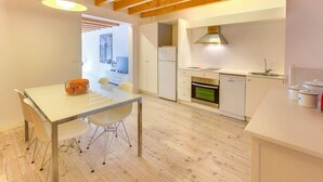 A modern kitchen with a dining area, wooden beams, white cabinetry, and a built-in oven. - URBAN SUITES 2 PALMA STANDARD by PriorityVillas (Palma de Mallorca)