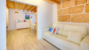 A cozy living area with a wooden ceiling, a stone wall, and a white sofa with decorative pillows. - URBAN SUITES 2 PALMA STANDARD by PriorityVillas (Palma de Mallorca)