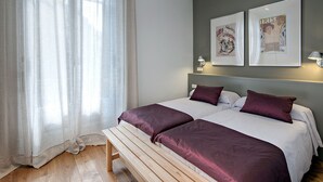 Ein Schlafzimmer mit zwei Betten, einer Bank und einem großen Fenster mit transparenten Vorhängen.