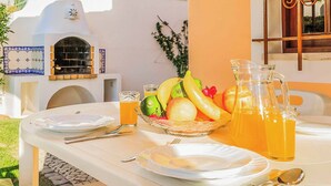 Une table mise pour le petit-déjeuner, avec des assiettes, des couverts, un panier de fruits et des carafes de jus d’orange.
