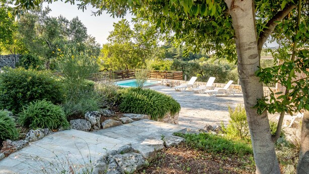 A stone pathway leading to a pool area with lounge chairs and a wooden deck.