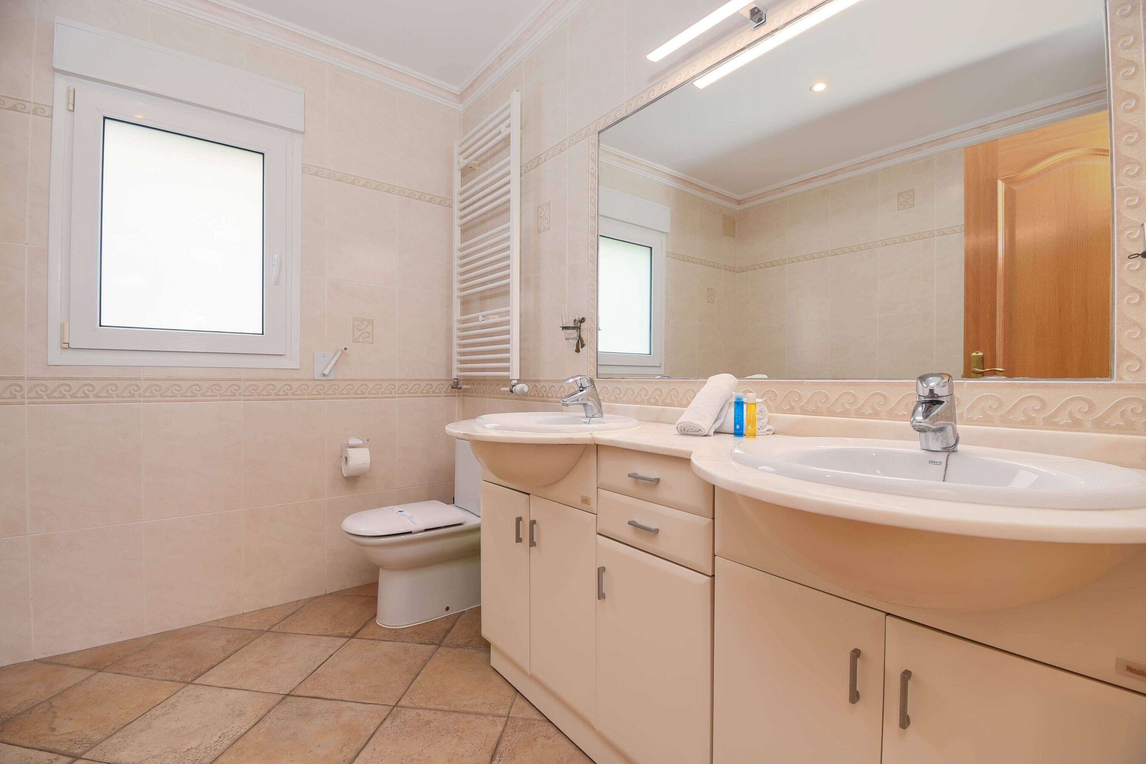 A bathroom with two sinks, a toilet, and a window.