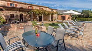 An outdoor patio with a stone table and chairs, a lounge area with sunbeds, and a building with a stone facade and wooden shutters. - Charming villa - 4km to beach and 2km to Old Town! (Palma de Mallorca)