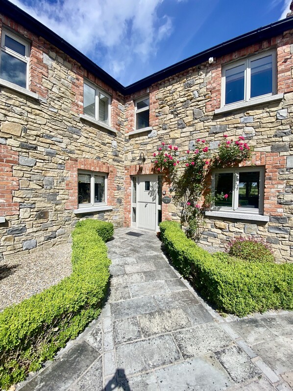 A stone building with a central entrance, windows, and a pathway leading to the door.