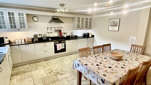 A kitchen with white cabinets, a dining table with a patterned tablecloth, and a tiled floor. - Beautiful 3 bedroom house in a delightfully landscaped and private courtyard (Navan)