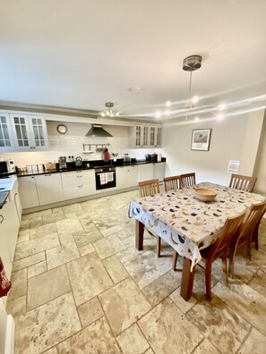 A kitchen with white cabinets, a dining table with a patterned tablecloth, and a tiled floor.