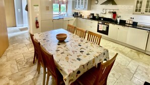 A kitchen with white cabinets, a dining table with a floral tablecloth, and a stone floor. - Beautiful 3 bedroom house in a delightfully landscaped and private courtyard (Navan)