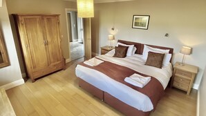 A bedroom with a large bed, wooden wardrobe, bedside tables, and a hanging light fixture. - Beautiful 3 bedroom house in a delightfully landscaped and private courtyard (Navan)