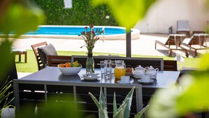 Un espace de restauration en plein air avec une table dressée pour le petit-déjeuner, un vase rempli de fleurs et une vue sur une piscine.