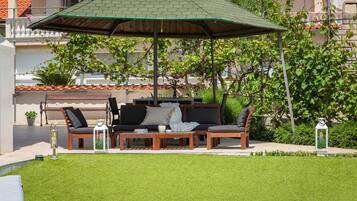 Un espacio al aire libre con mesa de madera, sillas y una sombrilla verde.
