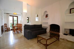 A living room with a sofa, a glass coffee table, a fireplace, a TV, and a dining area with chairs and a table.
