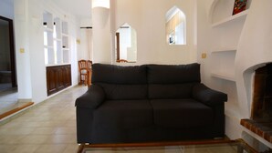 A living room with a dark sofa, wooden chairs, a fireplace, and white walls with built-in shelving. - PIVERD DEL GOLF 56 (Pals)
