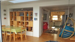 Ett rymligt vardagsrum med ett matbord, bokhyllor i trä, en röd soffa, en hängstol och ett kök i bakgrunden.