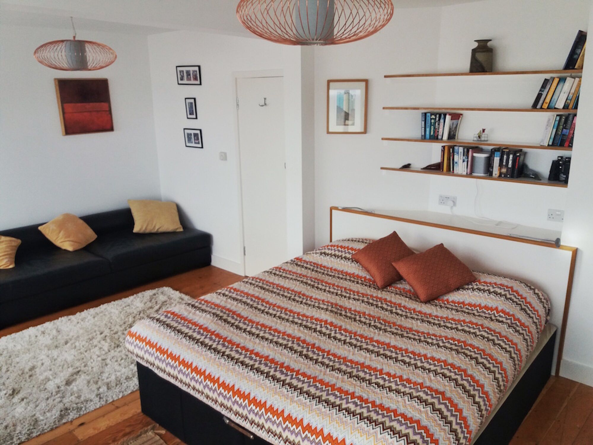 Ein modernes Schlafzimmer mit einem großen Bett, einer schwarzen Couch, einem Bücherregal und einer Pendelleuchte.