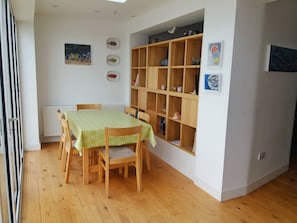 Ein Essbereich mit einem Tisch, der mit einer grünen Tischdecke bedeckt ist, Holzstühlen und einer an der Wand befestigten Holzregaleinrichtung.