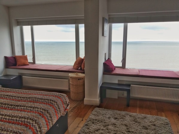 Ein Schlafzimmer mit großen Fenstern, einem Bett, einer Sitzbank und Meerblick.