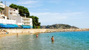 A coastal hotel with a pool area, a restaurant with blue awnings, and a rocky hillside in the background.