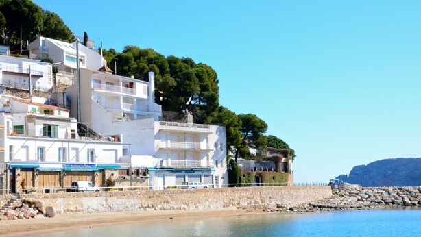 A coastal building with multiple balconies, a stone retaining wall, and a clear view of the sea.
