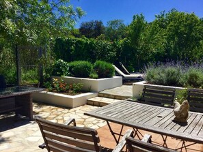 Eine Terrasse im Freien mit Steinböden, Holzmöbeln und Pflanzgefäßen mit verschiedenen Pflanzen.
