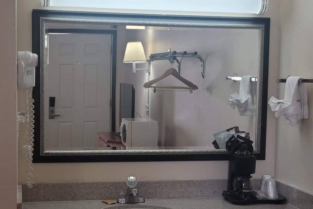 Un baño con un espejo grande, un lavamanos, un perchero para toallas y una toalla colgada.