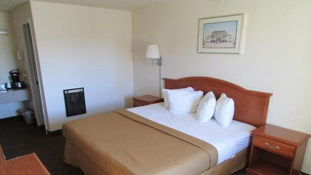 A hotel room with a large bed, a bedside table, a lamp, a trash bin, and a framed picture on the wall. - Western Inn (Green River)